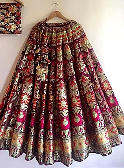 A heavy maroon and gold bridal lehenga on a hanger, back from cleaning